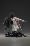 Right side view of Sadako levitating above a pile of videotapes, hugging her left leg, right leg bent, against a dark, lit background. (Prototype Shown) View 12